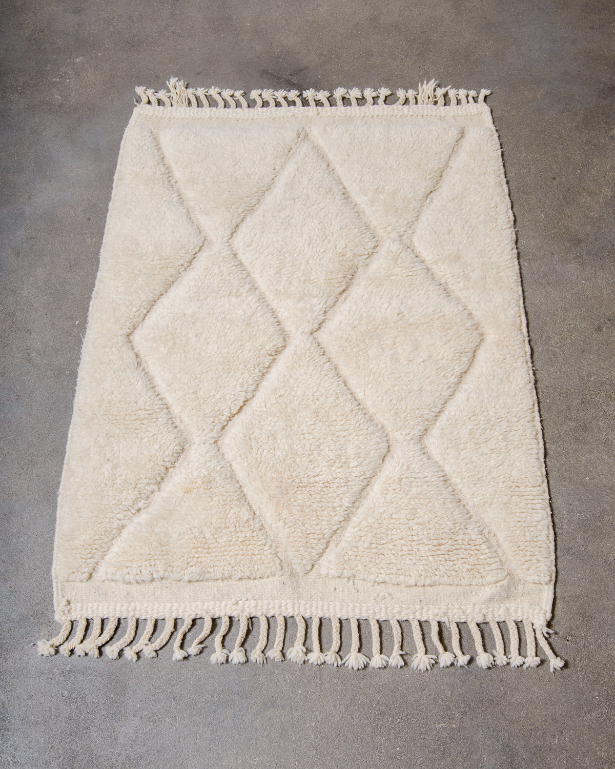 Beniourain rug in cream wool laying on concrete studio floor.